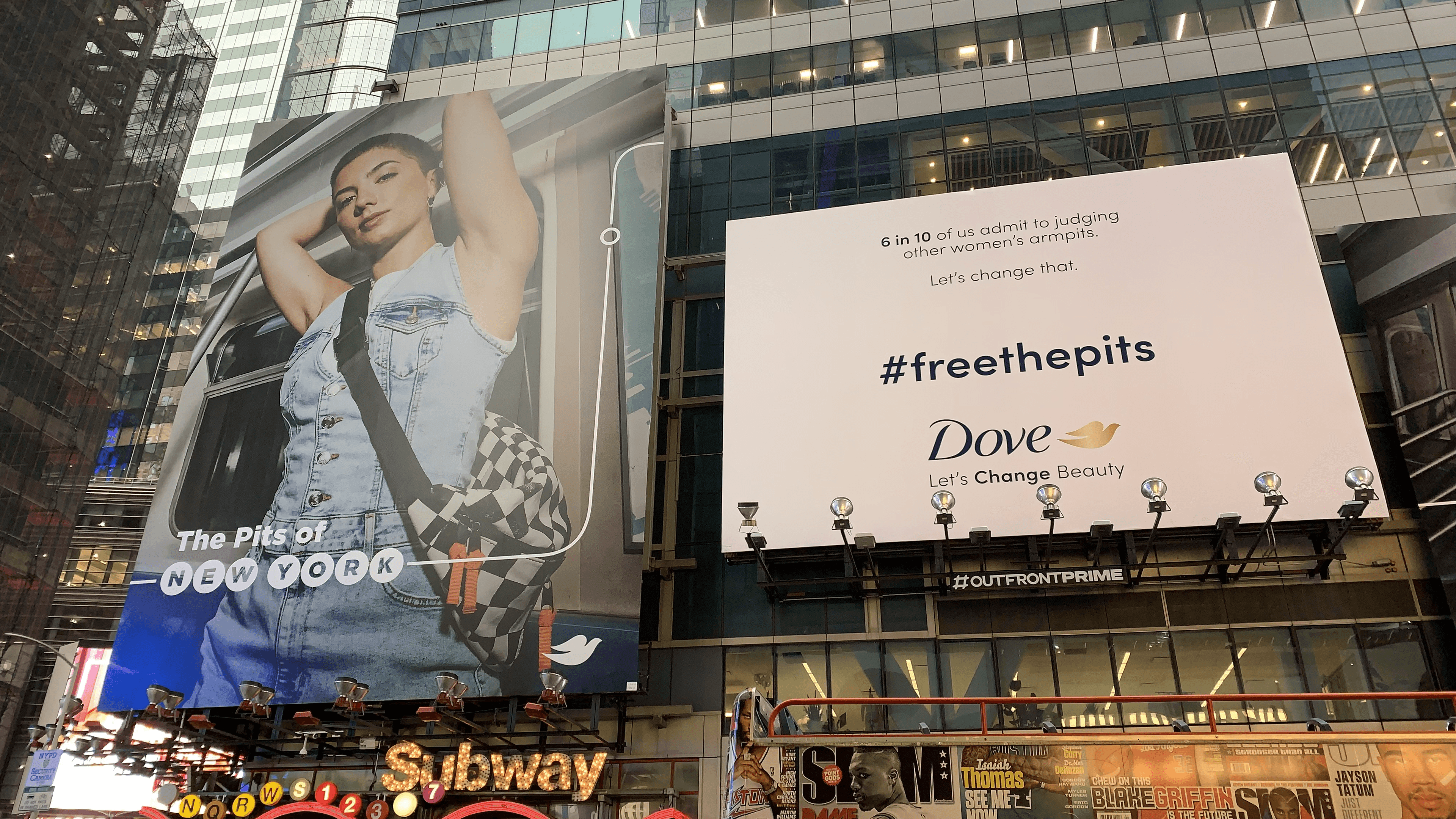 A street-level view of two Dove campaign billboards above a subway entrance. The billboard on the left shows a woman in a denim vest with her arms raised on a train. The billboard on the right is white with the text: "6 in 10 of us admit to judging other women's armpits. Let's change that. #freethepits."
